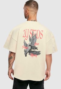 Camiseta oversize color crema con un gráfico de dos palomas. El texto dice "2Y STDS", "Paz", "Amor" y "Misericordia". Manga corta, corte relajado.
