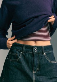 Pleteni tamnopurple džemper preko prugastog, uskog topa. Tamni traper suknja sa zatvaranjem na dva dugmeta i svijetlim šavovima, sa bočnim džepovima.