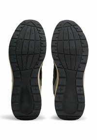 Black rubber soles with a textured pattern and beige accents; features ridges and grooves for traction, designed for durability and stability.