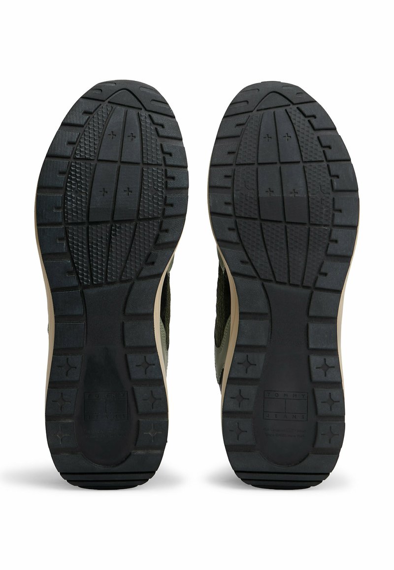 Black rubber soles with a textured pattern and beige accents; features ridges and grooves for traction, designed for durability and stability.