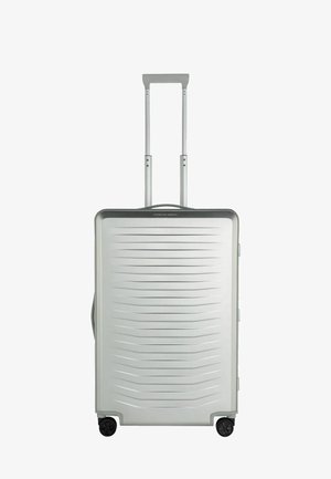 Valise rigide argentée avec des rainures horizontales, une poignée télescopique et quatre roues noires pour la mobilité. Poignée latérale pour le levage.