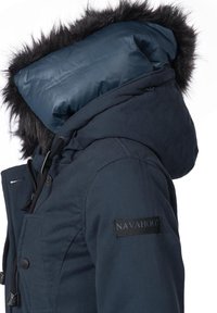 Navy blue jacket with a faux fur-lined hood, featuring a smooth inner lining, front buttons, adjustable drawstrings, and a logo patch.
