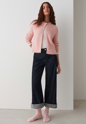 Pink knitted cardigan with round neckline and button closure, paired with dark wide-leg jeans and light pink ribbed socks.