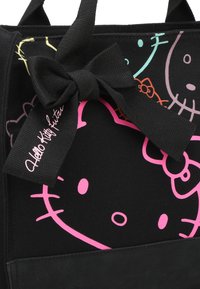 Borsa a tracolla nera in tela con un design della faccia di Hello Kitty rosa, accentuata da un fiocco nero e un'etichetta distintiva. Materiale resistente con finitura texturizzata.
