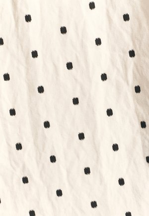 Tissu en coton avec un fond crème, présentant un motif répétitif de petits carrés noirs aux bords texturés. Rides visibles.