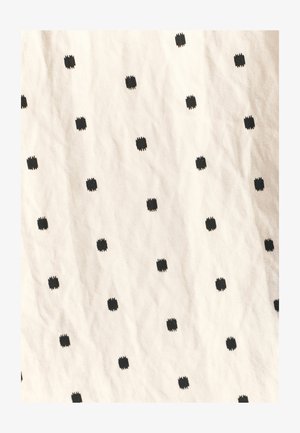 Tessuto di cotone con uno sfondo crema, caratterizzato da un motivo ripetuto di piccoli quadrati neri con bordi testurizzati. Pieghe visibili.