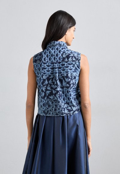 Blue patterned sleeveless vest with a high collar, featuring diverse textures and designs, paired with a dark blue skirt.