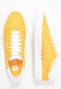 Gula canvas sneakers med vita gummisulor, vita snören och sidostripes. Har ett texturerat mönster på sulan och varumärke på tungan.