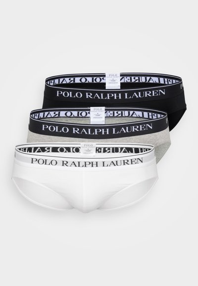Tri para raztegljivih bombažnih hlačk v beli, črni in sivi barvi, vsaka z brendiranim elastičnim pasom, na katerem je napis "POLO RALPH LAUREN" v črni barvi.