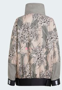 Giacca di colore beige chiaro con motivo floreale, rifiniture grigie e dettagli a strisce. Presenta un colletto alto e polsini elastici.