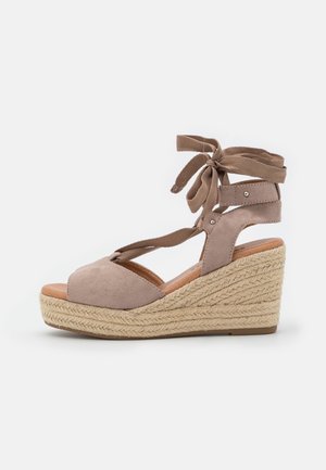 Sandale à talon compensé en suède beige avec semelle en jute tressé et brides de cheville nouées en un nœud.