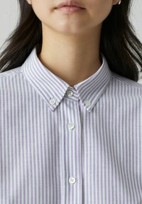 Camicia a righe violacee e bianche con colletto, caratterizzata da una texture di tessuto morbido e bottoni distintivi sul davanti.