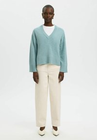 Light blue, knit sweater with a V-neck, ribbed hem and cuffs, paired with cream-colored wide-leg trousers and pointed white shoes.