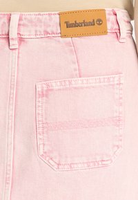 Shorts in denim rosa chiaro con una tasca posteriore rettangolare, caratterizzati da una finitura cucita. Un'etichetta in pelle marrone con il logo Timberland è visibile sopra la vita.