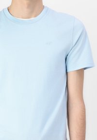 Ανοιχτό μπλε βαμβακερό μπλουζάκι με στρογγυλή λαιμόκοψη και κοντά μανίκια. Διαθέτει ένα μικρό, κεντημένο λογότυπο στο στήθος. Μαλακή υφή.