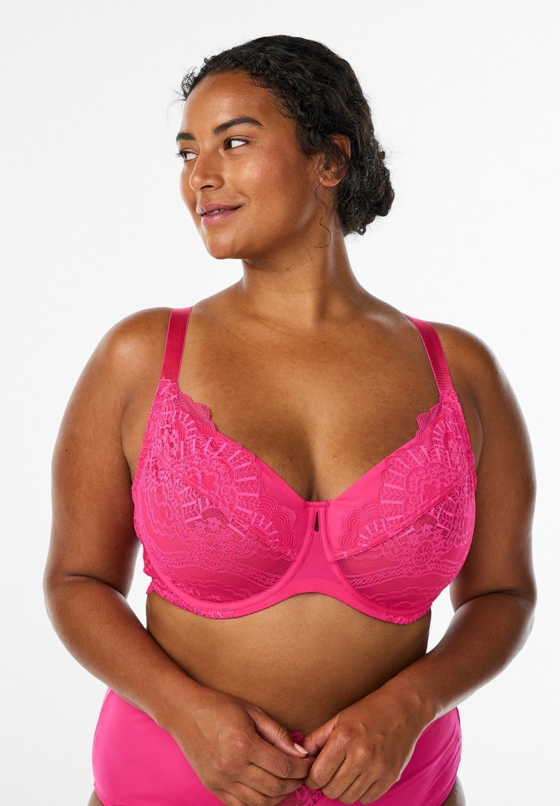 Rozā mežģīņu krūšturis ar platiem regulējamiem plecu siksnām, dekoratīvu apdari un ziedu rakstu uz kausiņiem. Apakšā gluda auduma apdare.