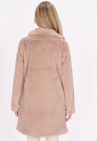 Cappotto in pelliccia sintetica beige chiaro, lungo fino al ginocchio, con collare a scialle, maniche lunghe e una texture morbida. La vista posteriore mostra un orlo arrotondato e liscio.