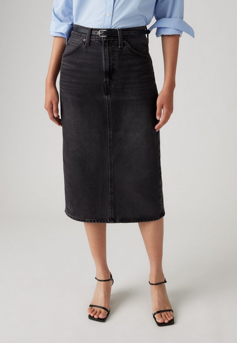 Black denim midi skirt with a straight cut, featuring front pockets, belt loops, and a subtle faded texture. Worn with black strappy heeled sandals.