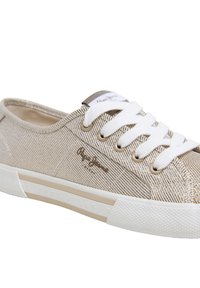 Beige lerretsneaker med teksturerte striper, hvite lisser og gummisåle. Har gullfarget logodetalj og subtil merkevare på siden.