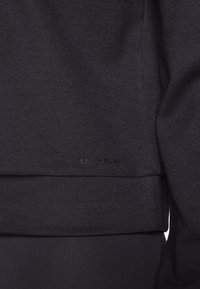 Gros plan sur l'ourlet d'un sweat-shirt en tissu noir avec une discrète broderie du logo "ONLY PLAY" près du bord inférieur.