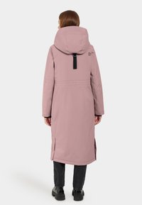 Cappotto lungo, rosa, con cappuccio, realizzato in materiale liscio e isolato. Presenta fessure laterali e un dettaglio a strappo nero sul retro.