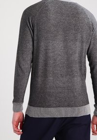 Szary sweter z dzianiny z prążkowanymi mankietami i dolnym wykończeniem, z teksturowanym wzorem i okrągłym dekoltem. Widok z tyłu pokazuje rękawy raglanowe.