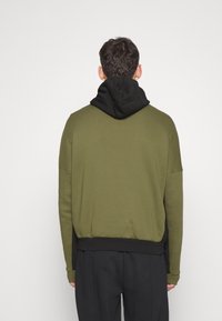 Olivgrön sweatshirt med svart huva, med en avslappnad passform, långa ärmar och ribbade muddar. Slätt tyg med matt yta.