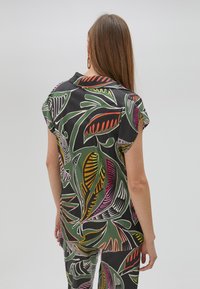 Camicia a maniche corte con colletto in tessuto nero, decorata da una vivace stampa di foglie in verde, rosa, rosso e giallo. Tessuto liscio, vestibilità comoda.