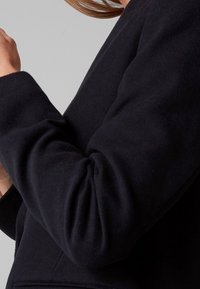 Sweat-shirt noir avec un tissu texturé, coupe ample et manches légèrement bouffantes. Les poignets sont côtelés, ajoutant du détail au design.