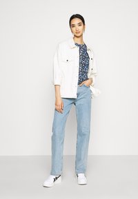 Giacca di denim, top floreale, jeans azzurri chiari e sneakers bianche con dettagli neri. Tra le caratteristiche ci sono bottoni e maniche arrotolate.