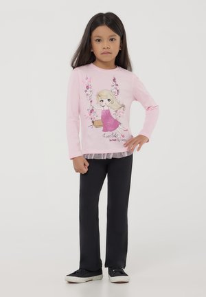 Camicia a maniche lunghe rosa chiaro con una grafica scintillante di una ragazza in abito rosa, abbinata a pantaloni neri e sneakers nere.