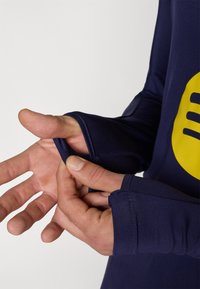 Navy long-sleeve shirt with a round neckline and thumbhole detail at the cuffs, featuring a large yellow graphic design on the front.