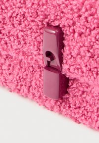 Ροζ υφασμάτινη επιφάνεια με υφή που μοιάζει με γούνα, με την ενσωμάτωση μοβ πλαστικού κλιπ στο σχέδιο.
