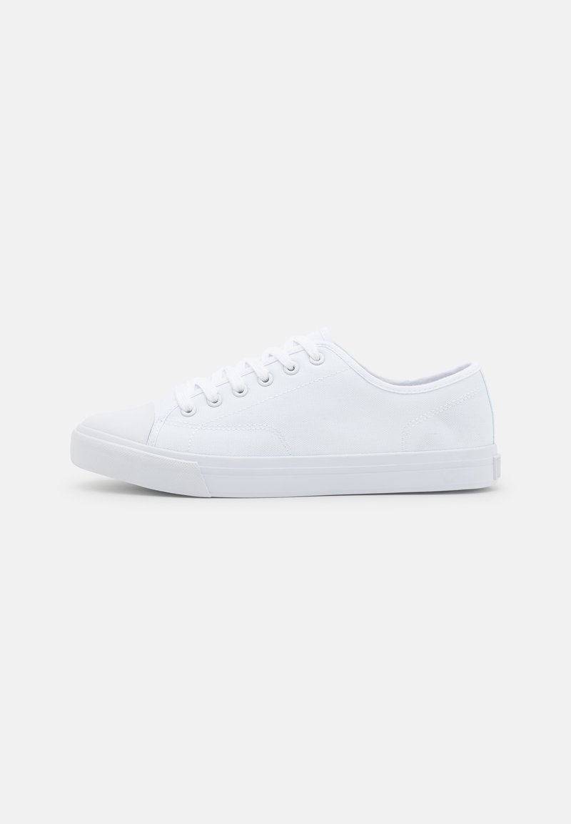 Zapatilla de lona blanca con puntera de goma, cordones redondos, diseño de corte bajo y tela texturizada. Presenta una suela de goma plana.