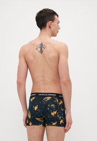 Schwarze Boxershorts mit floralem Muster in Grün und Gelb, mit einem schwarzen Bund, auf dem das Logo "JACK & JONES" zu sehen ist. Modell von hinten gezeigt.