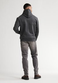 Sudadera gris con una gran capucha, textura suave y detalles en las costuras; combinada con jeans gris claro y zapatos marrón oscuro con una suela gruesa.