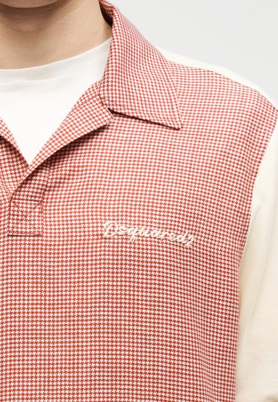 Gros plan sur un polo à motif pied-de-poule rouge et blanc avec un col et un logo "Dsquared2" brodé en blanc sur la poitrine.