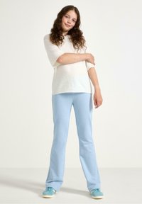 Weißer kurzärmliger Pullover kombiniert mit hellblauen Schlaghosen und blauen Sneakers, mit einer weichen Textur und lässiger Passform.