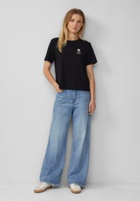 T-shirt en coton noir avec un col rond et un petit design graphique. Associe à un jean large en denim bleu clair et des baskets blanches.