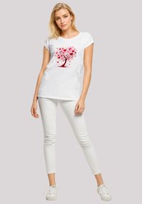 White t-shirt featuring a red tree design with heart-shaped leaves, paired with white skinny jeans and white sneakers.