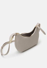 Borsa a tracolla in pelle beige con forma curva, zip dorata e tracolla rimovibile. Texture liscia con un design minimalista e apertura superiore.