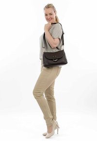 Borsa in pelle nera con una pattina curva, hardware metallico e una tracolla. Texture liscia con una grana sottile. Presenta un accento circolare.
