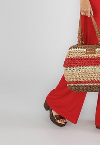 Vævet håndtaske i rød, beige og brun med en struktureret form, lysebrune håndtag og et logopræg. Teksturoverflade, letvægtsdesign.
