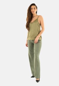 Camisola de seda verde oliva con encaje, combinada con pantalones rectos verdes oliva. Modelo lleva tacones negros de punta.