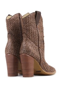 Botas de tobillo de cuero trenzado marrón con tacones de bloque de madera apilados y cremalleras laterales, fotografiadas desde atrás sobre un fondo blanco.