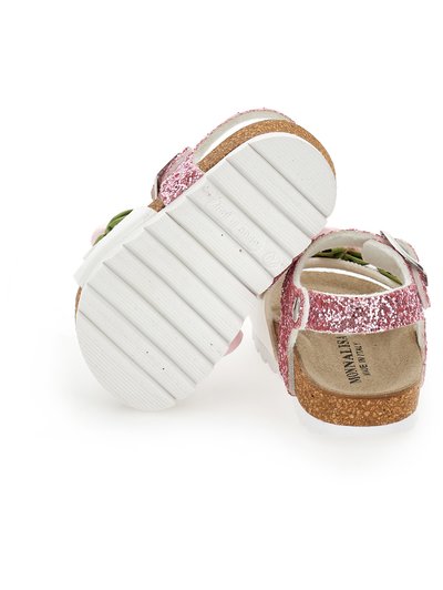 Sandalias de glitter rosa con correas blancas, suela de corcho y suela texturizada. Presenta un cierre con hebilla y un acento interior verde.