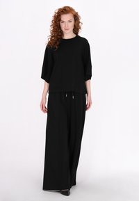 Top oversize nero con scollatura rotonda e maniche corte abbinato a pantaloni neri a gamba larga. Tessuto morbido, vestibilità rilassata, dettagli minimi.