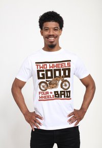Camiseta blanca con texto en marrón y rojo: "DOS RUEDAS BIEN CUATRO RUEDAS MAL," con un gráfico de una motocicleta. Mangas cortas, ajuste casual.