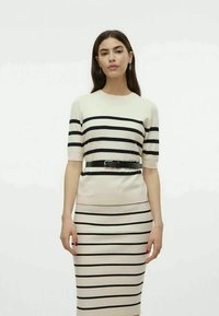 Vestido de malha com riscas horizontais pretas sobre um fundo creme, mangas curtas e uma silhueta ajustada com um cinto preto.