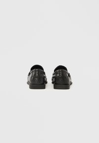 Μαύρα παπούτσια με υφή δερμάτινης σχεδίασης σε σχέδιο φίδι. Επίπεδη σόλα, στρογγυλεμένη μύτη και στυλ χωρίς πίσω μέρος. Ελάχιστα μεταλλικά στοιχεία και νότες.